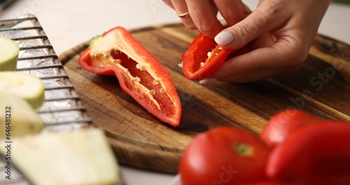Slicing vegetables. Female hands cut sweet Red Bell Pepper on a cutting board. Cooking in the kitchen. Food preparation. Close-up.