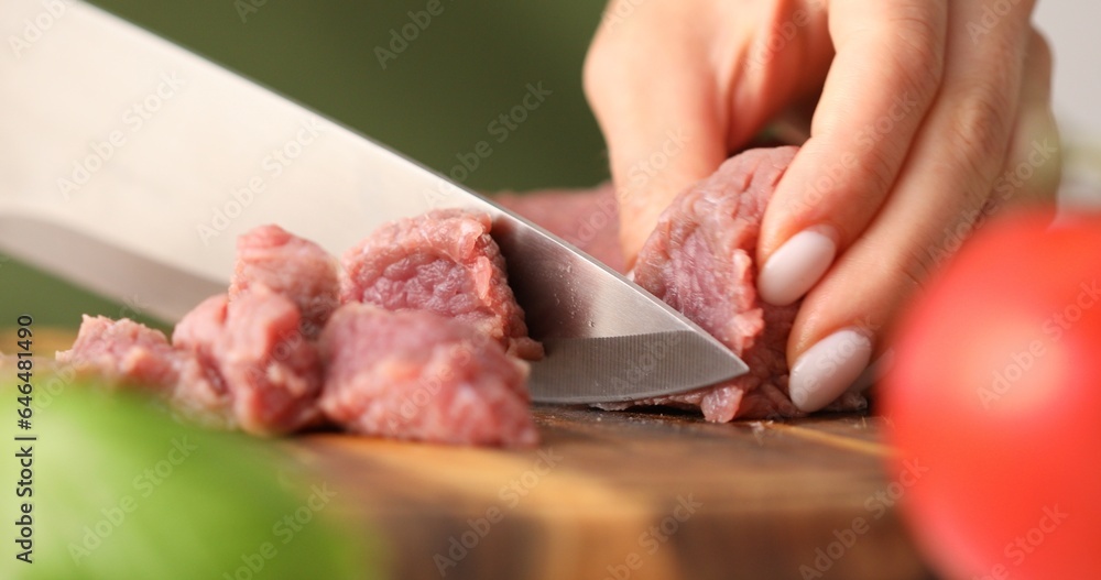 Cutting raw meat. Female hands cut fresh beef on a wooden chopping board. Cooking in the kitchen. Food preparation.