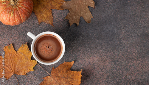 Cup of coffee next to autumn leaves and pumpkin on brown background, Top view