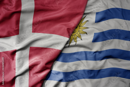 big waving national colorful flag of denmark and national flag of uruguay .