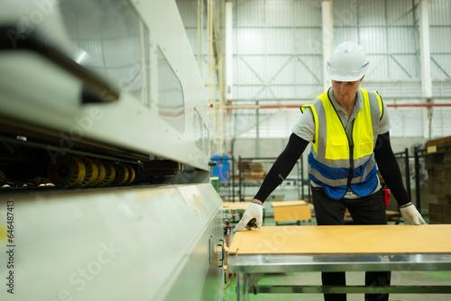 Portrait of a male worker working on a conveyor belt in a paper factory. Measuring and inspecting the paper coming out of the machine.