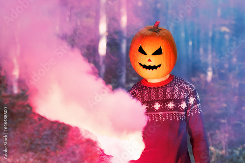 Portrait of adult person with Halloween pumpkin on head in a woodland night with colourful smoke. Halloween Jack-o-lantern funny party.