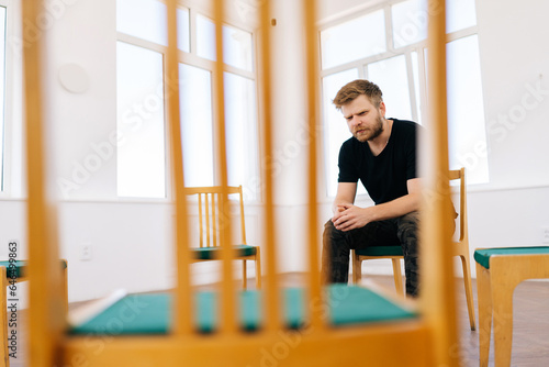 Remote view of depressed male soldier speaking about trauma during group psychotherapy session. Young bearded man veteran talking during PTSD support group. Concept of mental health  psychotherapy.