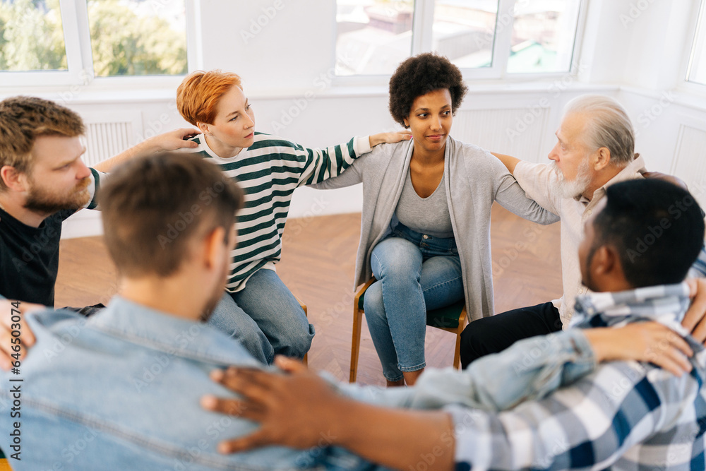 High-angle view of multicultural and different ages group of addicted people discuss problems and together holding shoulders each other on therapy sitting on chairs in circle. Concept of mental health High-angle view of multicultural and different ages group of addicted people discuss problems and together holding shoulders each other on therapy sitting on chairs in circle. Concept of mental health