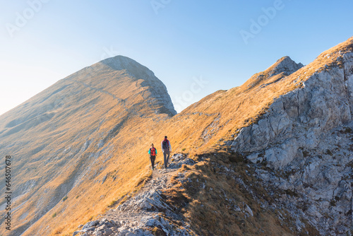 Hiking couple, a young woman with trekking poles, and a fit man skillfully walking over a rocky trail on a mountain range