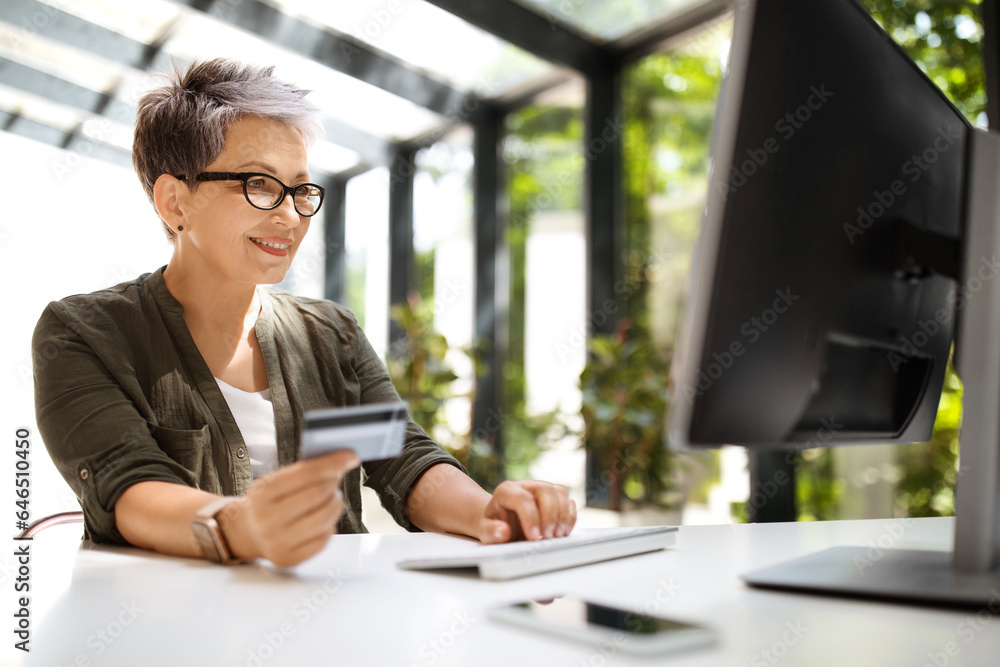 Mature woman holding credit card and using computer Mature woman holding credit card and using computer