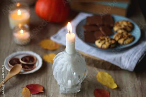 Cup of tea or coffee, plate with desserts, dried oranges, bowl of grapes, scented candles, vintage books, pumpkins and autumn leaves on the table. Autumnal hygge. Selective focus.