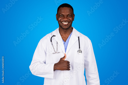 Positive young african american guy doctor in white coat show thumb up, approving ad and offer