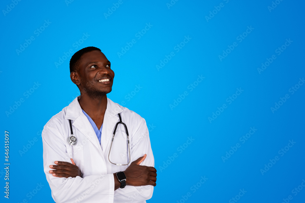 Positive young african american doctor in white coat with crossed arms on chest looks at copy space Positive young african american doctor in white coat with crossed arms on chest looks at copy space