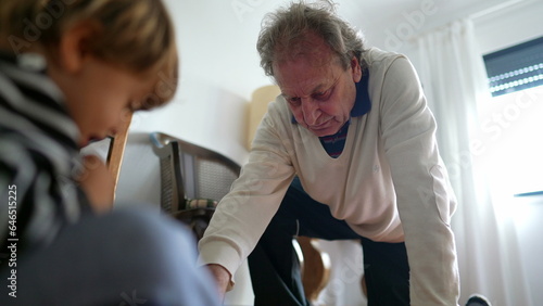 Grandfather playing with grandson in bedroom floor, senior man on his knees interacting with grandchild, inter-generational authentic lifestyle scene