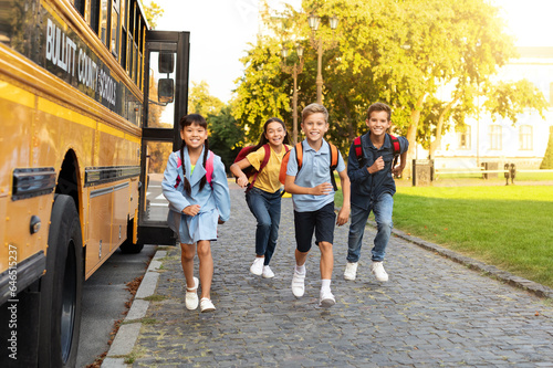 Group of happy children with backpacks running from school bus