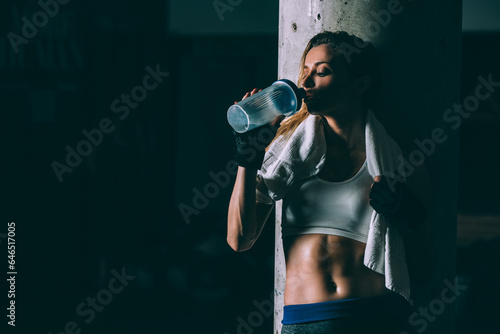 Fit blonde tired woman resting and drinking after training working out in Gym