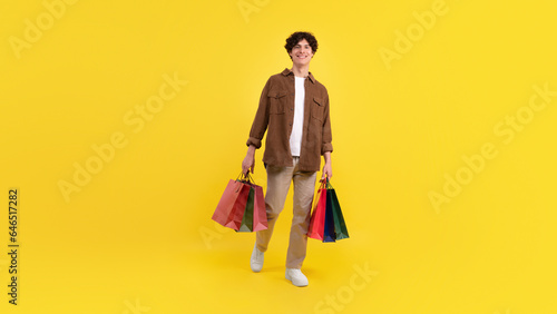 Cheerful guy holding many paper bags smiling on yellow background