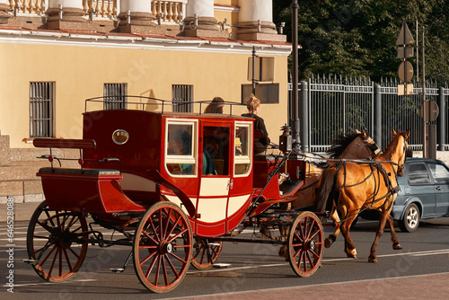 Photography A red carriage drawn by two horses rides along a city road