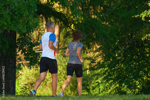 A middle-aged man and woman run through the summer forest. Childfree family doing sports together.