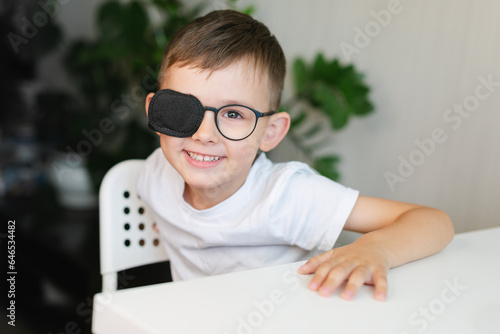 A happy boy with an occluder on his glasses is smiling.
