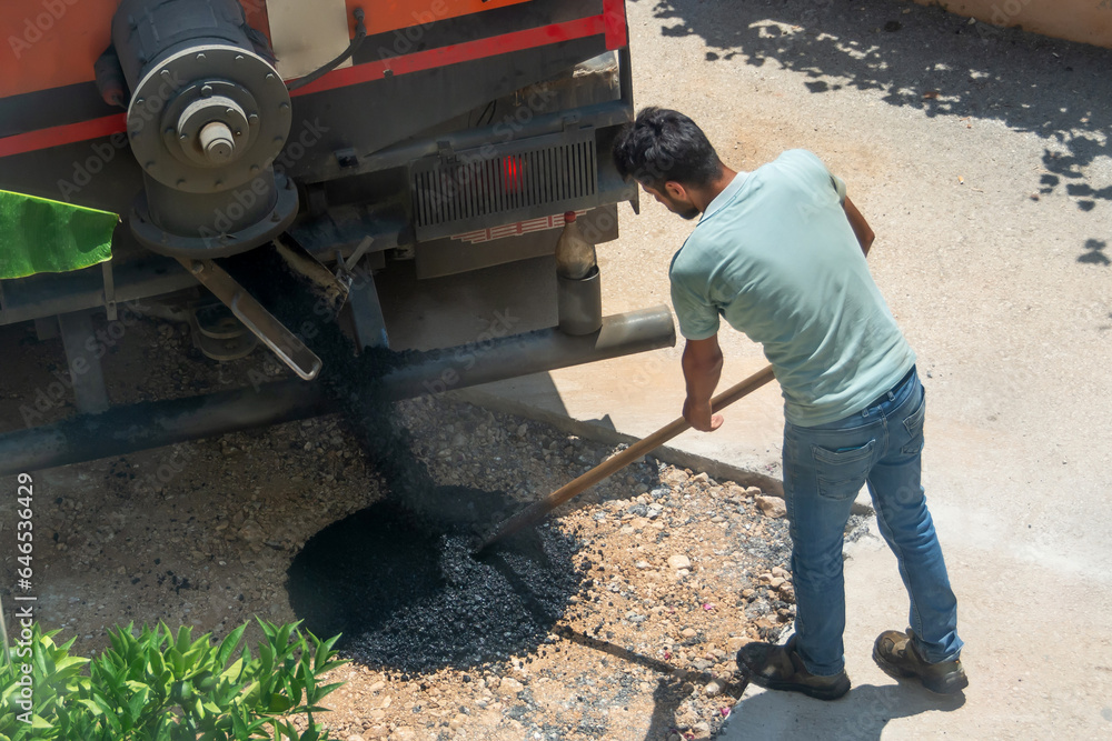 Worker pours and levels fresh asphalt from a truck to be laid onto the street road surface. Worker pours and levels fresh asphalt from a truck to be laid onto the street road surface.