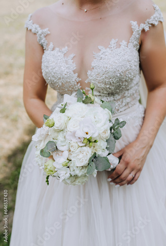 The bride in a white dress holds a bouquet with flowers, roses in her hands outdoors. Wedding portrait, photography.