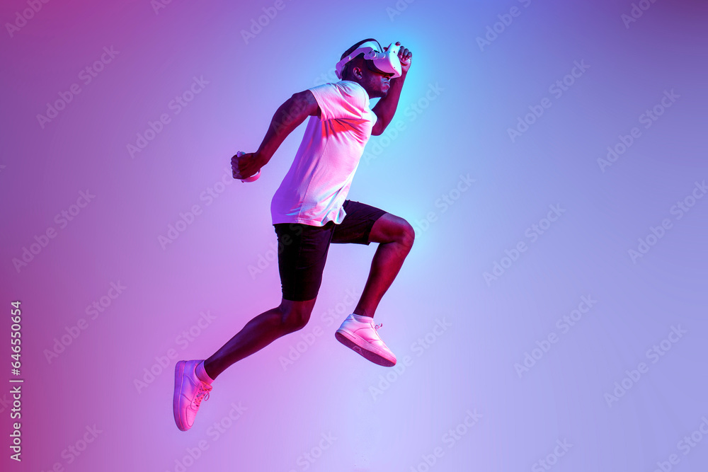 african american athletic man jumping in virtual reality glasses in neon lighting, the guy athlete runs and trains