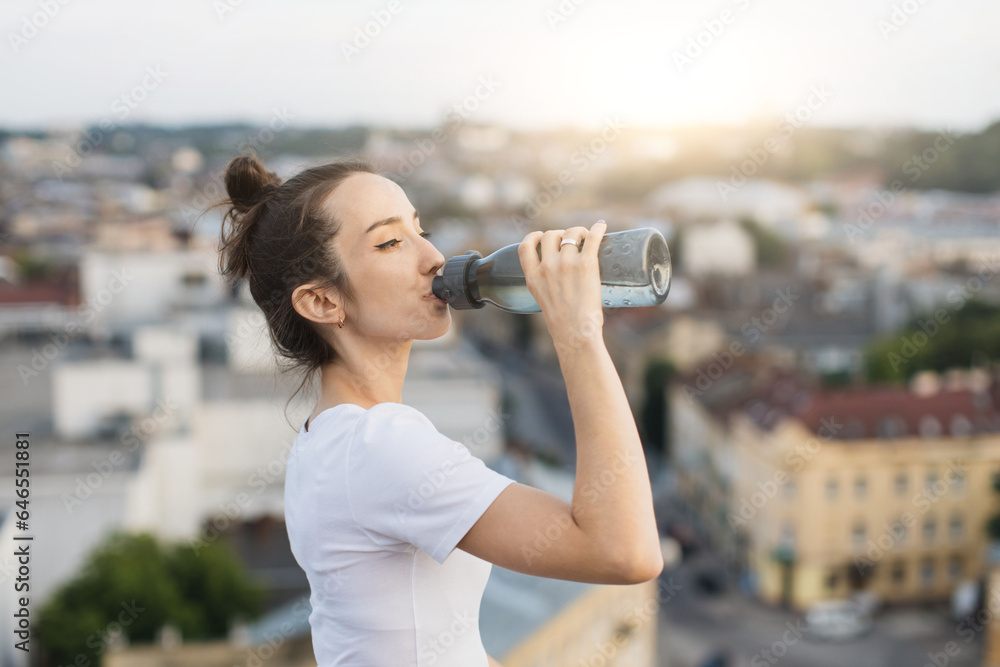 Female drinking water from sports bottle on roof terrace Female drinking water from sports bottle on roof terrace