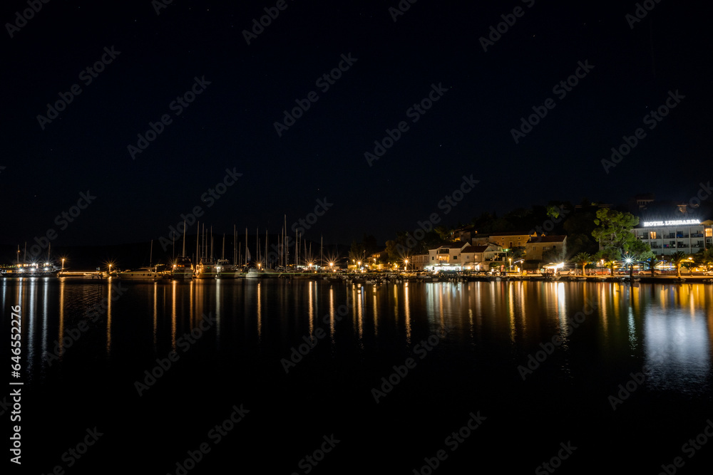 Night photo of small town of Lumbarda located on Korcula island, Croatia with houses and anchored boats reflected in smooth sea water