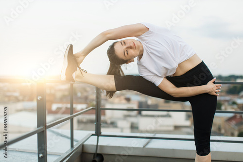 Female stretching muscles while exercising on evening roof