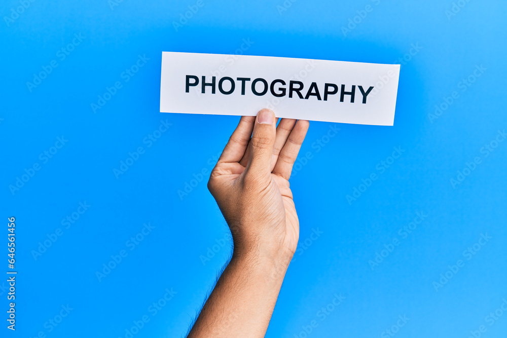 Hand of caucasian man holding paper with photography word over isolated blue background Hand of caucasian man holding paper with photography word over isolated blue background