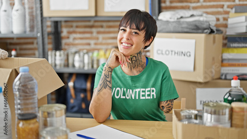 Hispanic woman with amputee arm volunteer smiling confident sitting on table at charity center