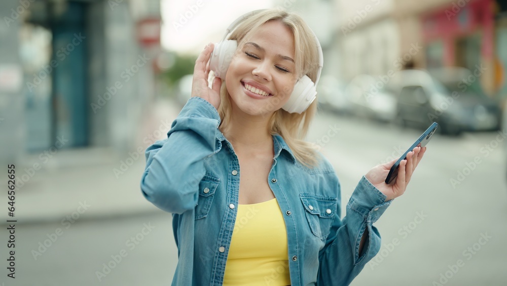 Young blonde woman smiling confident listening to music at street