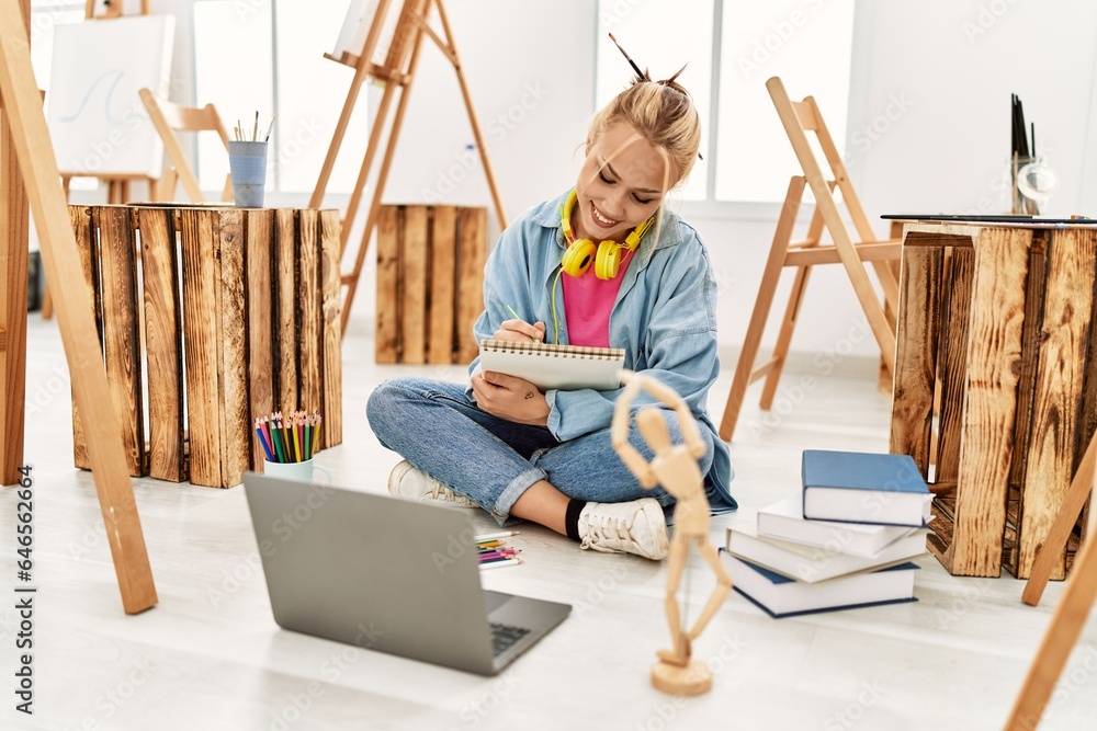 Young caucasian woman artist drawing on notebook sitting on floor at art studio