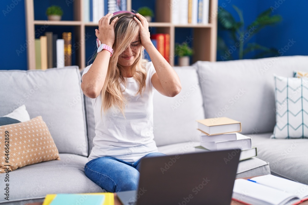 Young blonde woman studying using computer laptop at home suffering from headache desperate and stressed because pain and migraine. hands on head. Young blonde woman studying using computer laptop at home suffering from headache desperate and stressed because pain and migraine. hands on head.