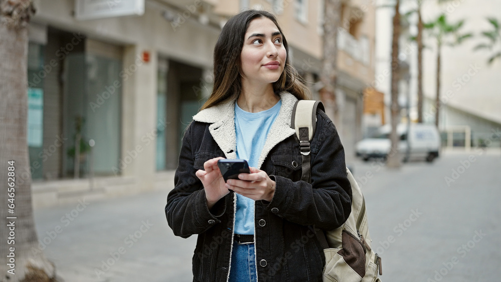 Obraz premium Young beautiful hispanic woman student smiling confident using smartphone at street