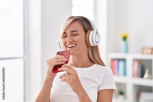 Young blonde woman listening to music singing song at bedroom