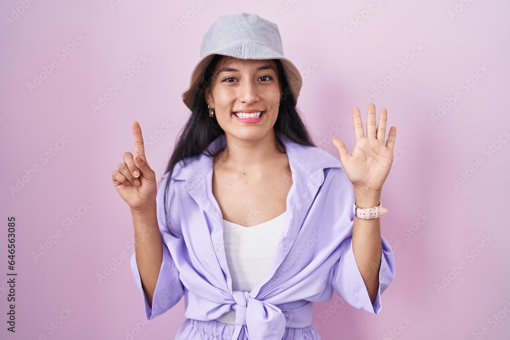 Young hispanic woman standing over pink background wearing hat showing and pointing up with fingers number six while smiling confident and happy. Young hispanic woman standing over pink background wearing hat showing and pointing up with fingers number six while smiling confident and happy.