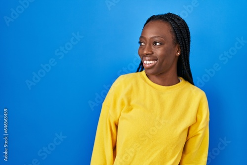 Beautiful black woman standing over blue background looking away to side with smile on face, natural expression. laughing confident. © Krakenimages.com