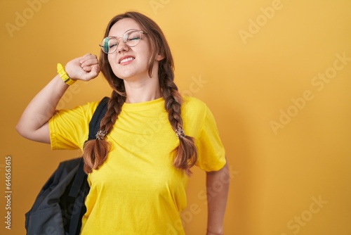 Young caucasian woman wearing student backpack over yellow background stretching back, tired and relaxed, sleepy and yawning for early morning © Krakenimages.com