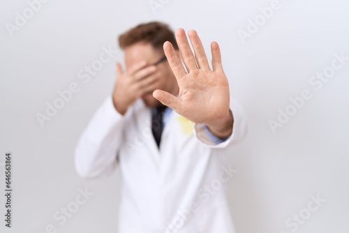 Middle age doctor man with beard wearing white coat covering eyes with hands and doing stop gesture with sad and fear expression. embarrassed and negative concept.