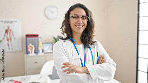 Young beautiful hispanic woman doctor smiling confident standing with arms crossed gesture at clinic