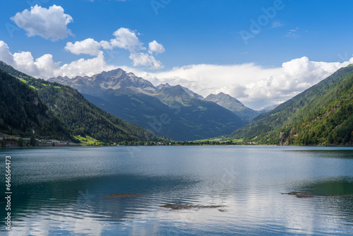 Swiss alpine lake in the mountains, Poschiavo (Miralago), Switzerland. Bernina massif peaks in the background of the green valley, blue sky with clouds. © Andrea