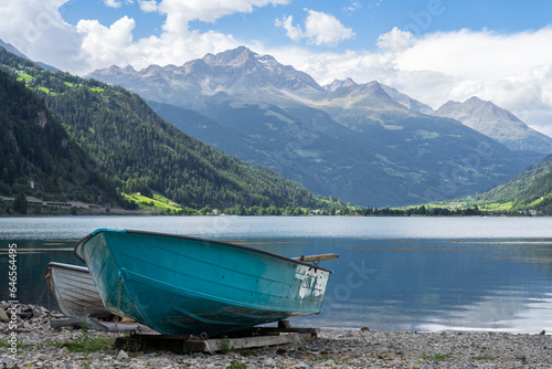 Swiss alpine lake in the mountains, turquoise boat in the foreground. Bernina massif peaks in the background, blue sky with clouds. Poschiavo (Miralago), Switzerland.  photo