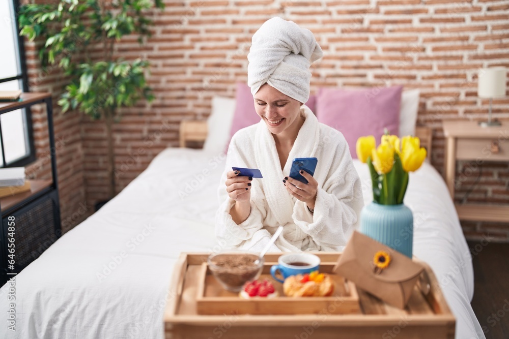 Young blonde woman shopping with smartphone and holding credit card having breakfast at bedroom Young blonde woman shopping with smartphone and holding credit card having breakfast at bedroom