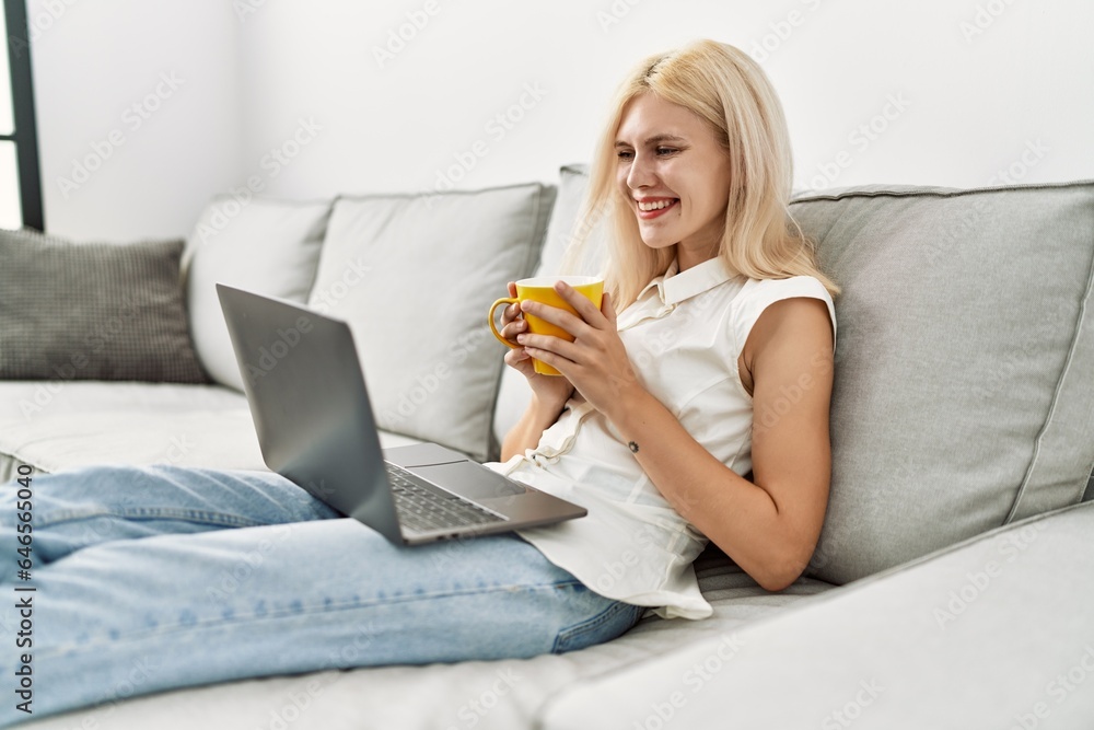 Young blonde woman using laptop drinking coffee at home Young blonde woman using laptop drinking coffee at home