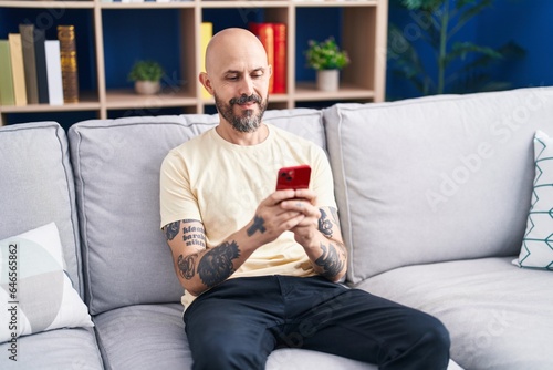 Young bald man using smartphone sitting on sofa at home © Krakenimages.com