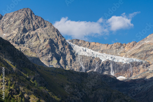 Bignami mountain hut and Fellaria Glacier with waterfall in the background, rocky peak with soft warm light, blue sky with cloud. Valmalenco mountains landscape, Italian Alps. Bernina massif photo