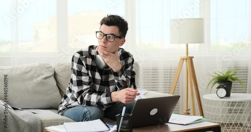 Seated on the sofa, a man displays signs of boredom as he tackles tasks from home. The atmosphere reflects a lack of engagement and monotony, capturing the challenges of maintaining focus. photo