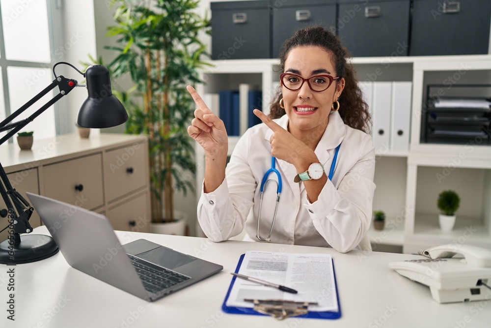 Young hispanic woman wearing doctor uniform and stethoscope pointing aside worried and nervous with both hands, concerned and surprised expression Young hispanic woman wearing doctor uniform and stethoscope pointing aside worried and nervous with both hands, concerned and surprised expression