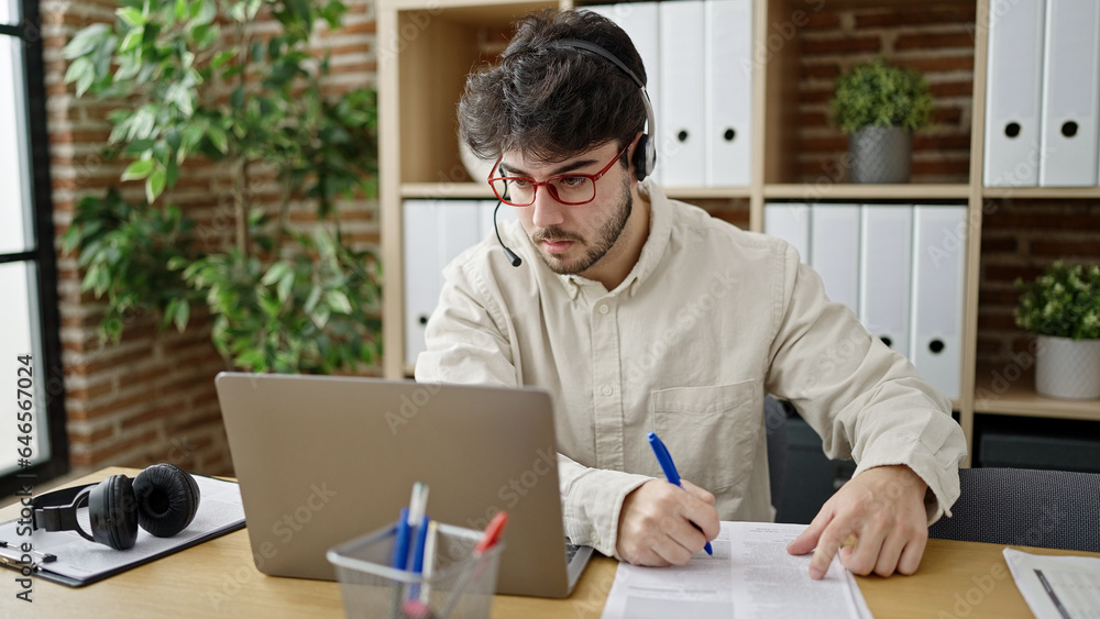 Young hispanic man call center agent writing notes speaking at office Young hispanic man call center agent writing notes speaking at office