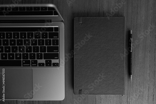 fotografia superior em preto e branco computador aberto ao lado de bloco de notas sobre mesa com espaço livre para texto photo