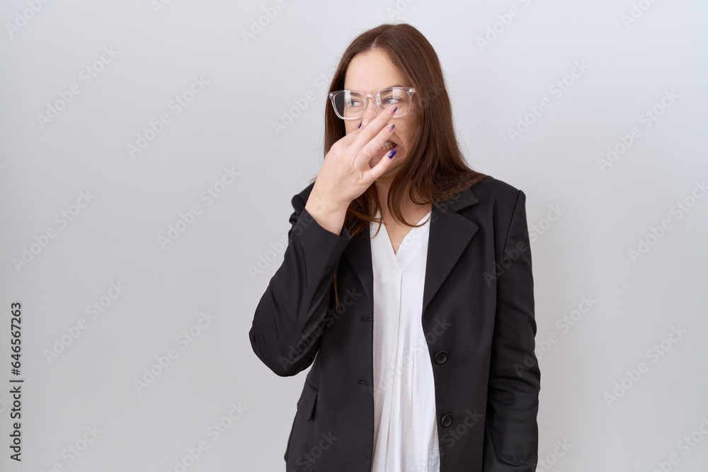 Beautiful brunette woman wearing business jacket and glasses smelling something stinky and disgusting, intolerable smell, holding breath with fingers on nose. bad smell Beautiful brunette woman wearing business jacket and glasses smelling something stinky and disgusting, intolerable smell, holding breath with fingers on nose. bad smell