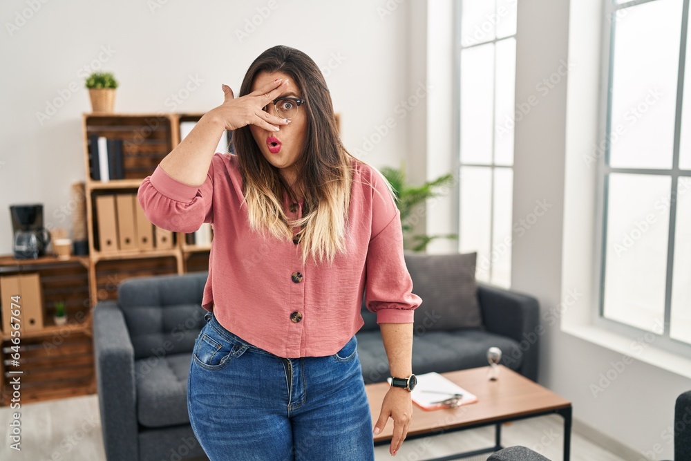 Young hispanic woman working at the office wearing glasses peeking in shock covering face and eyes with hand, looking through fingers afraid Young hispanic woman working at the office wearing glasses peeking in shock covering face and eyes with hand, looking through fingers afraid